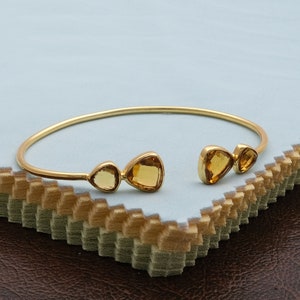 Op de afbeelding: Een gouden armband met drie citrien edelstenen. De armband is open en heeft een eenvoudig ontwerp.