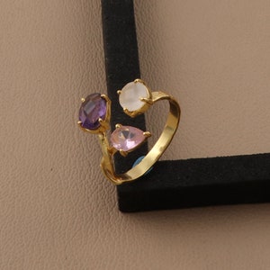 May include: Gold ring with three gemstones: a purple oval, a pink teardrop, and a white round stone.