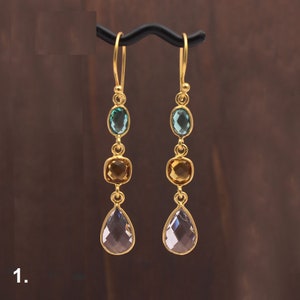 May include: Gold earrings with three gemstone drops. The top drop is a light blue oval, the middle drop is a square of amber, and the bottom drop is a teardrop of clear quartz.