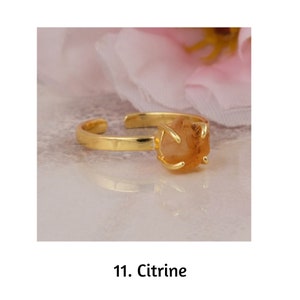 May include: A gold-colored adjustable ring featuring a raw, light orange citrine gemstone. The ring's band is smooth and open, with the citrine held in place by four prongs. The text "11. Citrine" is at the bottom of the image.