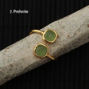 May include: A gold-toned ring featuring two square, light green gemstones. The ring's design is open, with the gemstones positioned on opposite sides of the finger. The text "7. Prehnite" is visible in the image.
