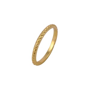 May include: A gold-colored ring with a textured, geometric pattern around the band. The ring is thin and appears to be made of metal. The ring is set against a white background.