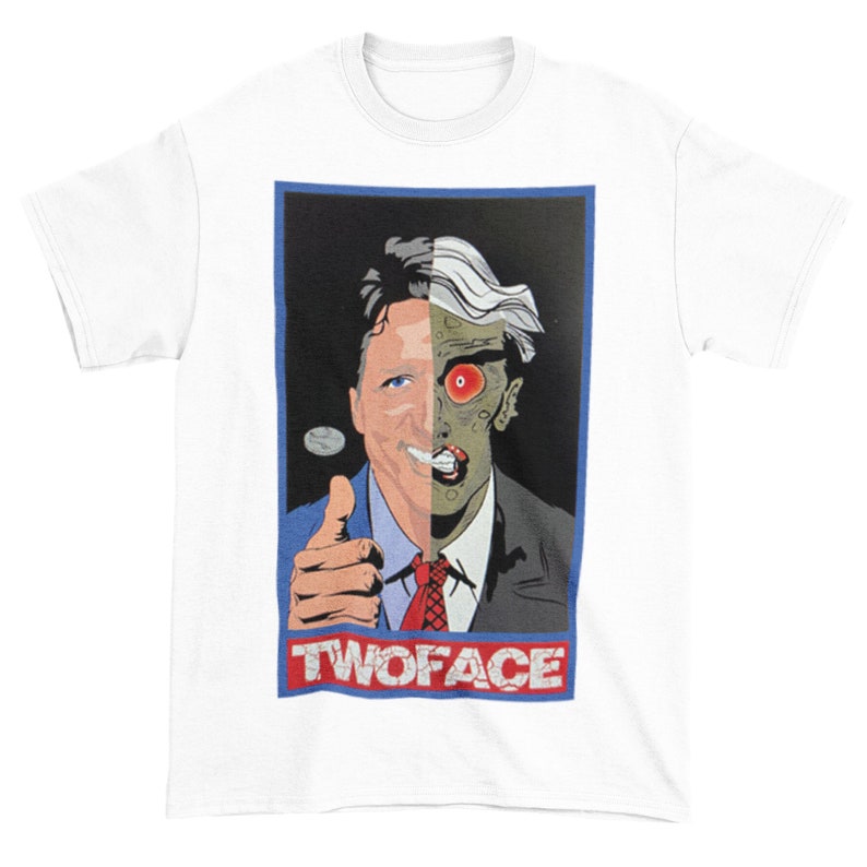 May include: A white t-shirt with a graphic of a man with two faces. One side of the face is a normal human face, and the other side is a grotesque, monstrous face. The graphic is in a red, white, and blue frame with the text "TWOFACE" at the bottom.