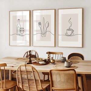 May include: Three minimalist line art prints in wooden frames, featuring a wine bottle and glass, a fork, knife, and spoon, and a steaming cup of coffee. The prints are hung on a white wall above a wooden dining table with wicker chairs.