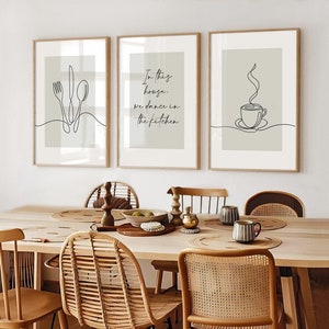 Peut inclure: Trois impressions d'art encadr&eacute;es avec des dessins au trait d'une fourchette, d'un couteau, d'une cuill&egrave;re, d'une tasse &agrave; caf&eacute; et le texte "In this house, we dance in the kitchen." Les impressions sont dans des cadres en bois.