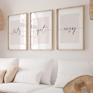 Peut inclure: Trois impressions encadrées avec un fond rose clair et une calligraphie noire. Les impressions indiquent "let's get cosy" de gauche à droite.