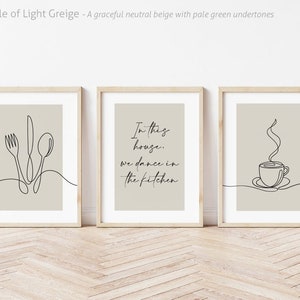 Peut inclure: Trois impressions d'art encadr&eacute;es avec un fond beige clair et un cadre en bois. Les impressions pr&eacute;sentent des dessins au trait minimalistes de couverts, une tasse &agrave; caf&eacute; et le texte "In this house, we dance in the kitchen."