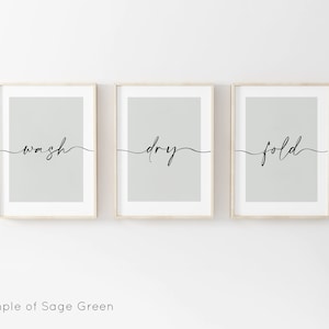 May include: Three framed prints with a sage green background and black calligraphy. The prints read "wash", "dry", and "fold" in a cursive font.