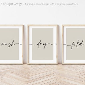 May include: Three framed prints with a light beige background and black cursive text. The prints read "wash", "dry", and "fold".