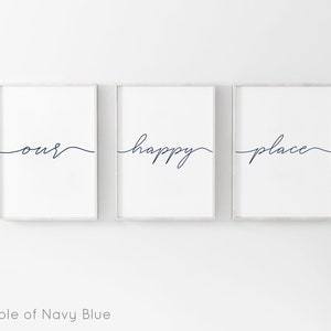 May include: Three framed prints with the words "our", "happy", and "place" written in a cursive script in navy blue. The prints are hung on a white wall.