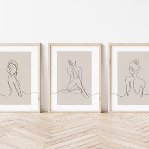 May include: Set of three minimalist line art prints featuring a woman in different poses. The prints are framed in natural wood frames and have a beige background.