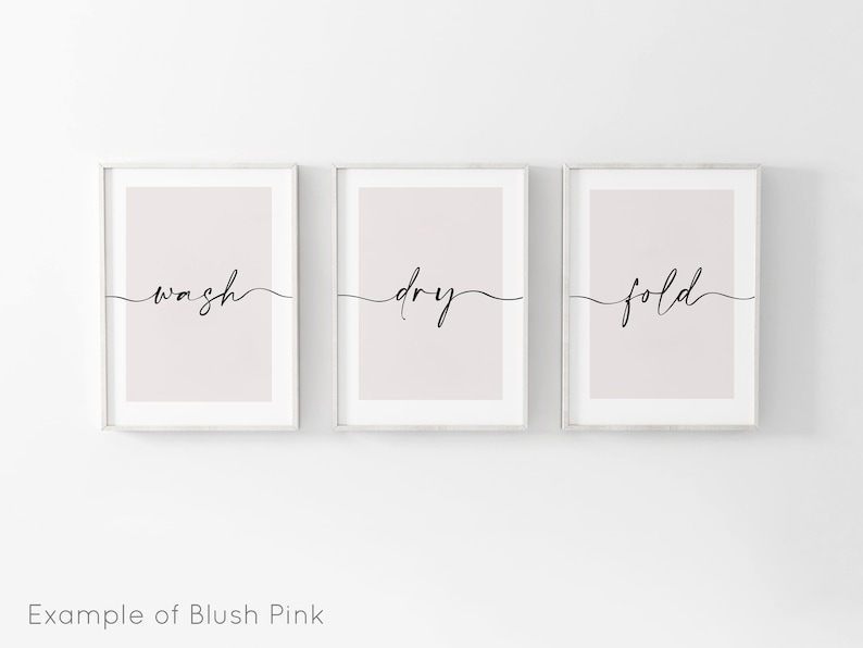 May include: Three framed prints with a blush pink background and black calligraphy. The prints read "wash", "dry", and "fold" in a cursive font.