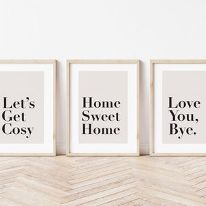 May include: Three framed prints with white backgrounds and black text. The first print says "Let's Get Cosy", the second print says "Home Sweet Home", and the third print says "Love You, Bye."