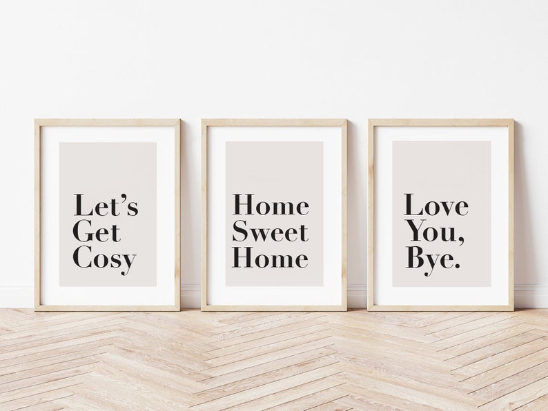 May include: Three framed prints with white backgrounds and black text. The first print says "Let's Get Cosy", the second print says "Home Sweet Home", and the third print says "Love You, Bye."