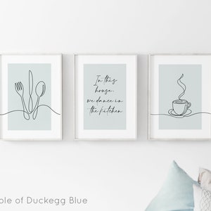 Peut inclure: Trois impressions d'art encadr&eacute;es avec des dessins au trait minimalistes. Les impressions pr&eacute;sentent une fourchette, un couteau et une cuill&egrave;re ; le texte "In this house, we dance in the kitchen" ; et une tasse de caf&eacute;. Le fond est bleu canard.