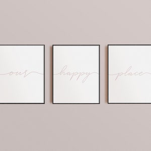 May include: Three framed prints with the words "our", "happy", and "place" written in cursive script. The prints are hung on a light pink wall.