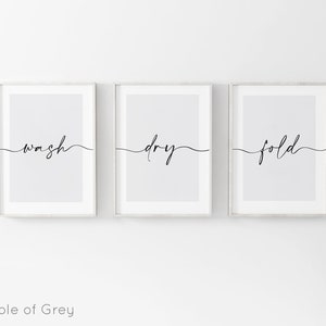 May include: Three framed prints with the words "wash", "dry", and "fold" written in a cursive font on a light gray background.