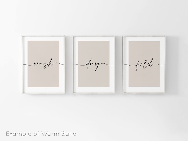 May include: Three framed prints with a light brown background and white frames. The prints have the words "wash", "dry", and "fold" written in black cursive.