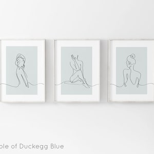 May include: Three framed prints with a light blue background and black line drawings of women in various poses. The prints are arranged in a row.