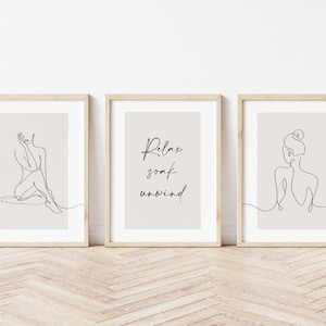May include: Three minimalist line art prints in wooden frames. The left and right prints feature a single line drawing of a person. The center print features the text "Relax soak unwind" in a simple font.