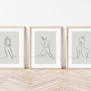 May include: Three minimalist line art prints featuring female figures in various poses. The prints are framed in light wood and have a light gray background.