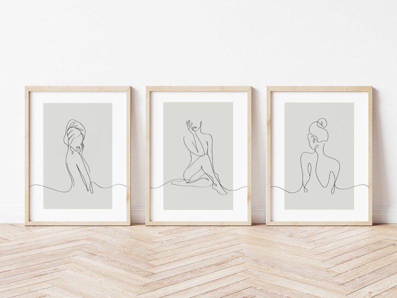 May include: Three minimalist line art prints featuring female figures in various poses. The prints are framed in light wood and have a light gray background.