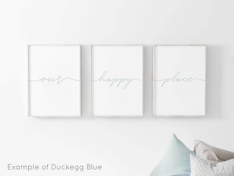 May include: Three white framed prints with the words "our", "happy", and "place" written in a cursive script in a light blue color. The prints are hung on a white wall.