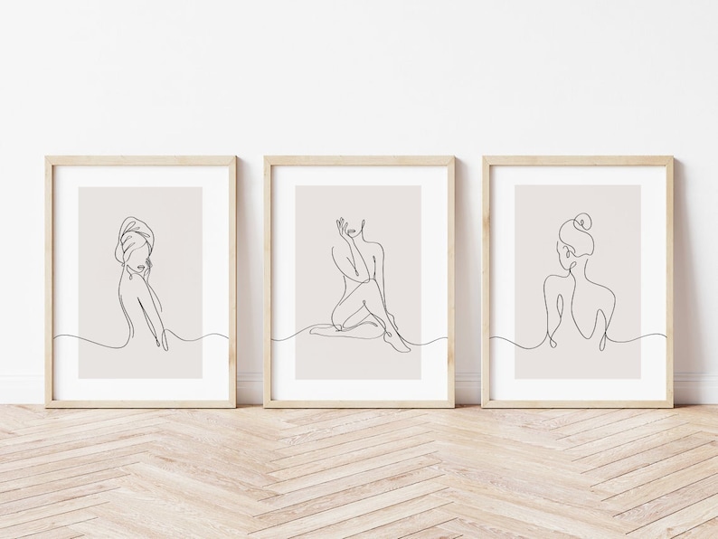 May include: Set of three minimalist line art prints featuring female figures in various poses. The prints are framed in light wood frames and have a beige background.