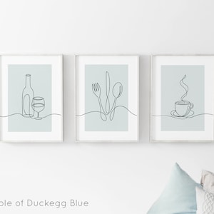 May include: Three minimalist line art prints in white frames with a light blue background. The prints depict a bottle of wine and a glass, a fork, knife, and spoon, and a steaming cup of coffee.