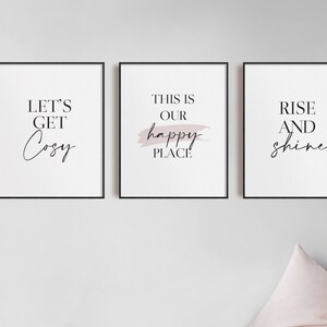 May include: Three framed prints with black frames and white backgrounds. The prints feature the text "Let's Get Cozy", "This is Our Happy Place", and "Rise and Shine". The middle print has a pink brushstroke behind the text.