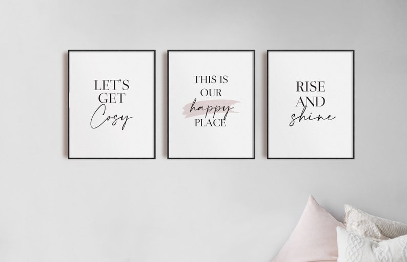 May include: Three framed prints with black frames and white backgrounds. The prints feature the text "Let's Get Cozy", "This is Our Happy Place", and "Rise and Shine". The middle print has a pink brushstroke behind the text.