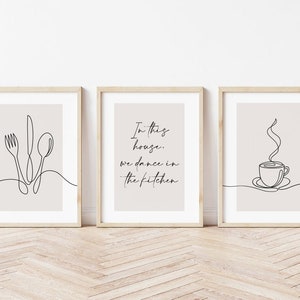 Peut inclure: Ensemble de trois impressions d'art encadr&eacute;es avec des dessins au trait minimalistes. L'une repr&eacute;sente une fourchette, un couteau et une cuill&egrave;re. Une autre dit "In this house, we dance in the kitchen." La troisi&egrave;me repr&eacute;sente une tasse de caf&eacute;.