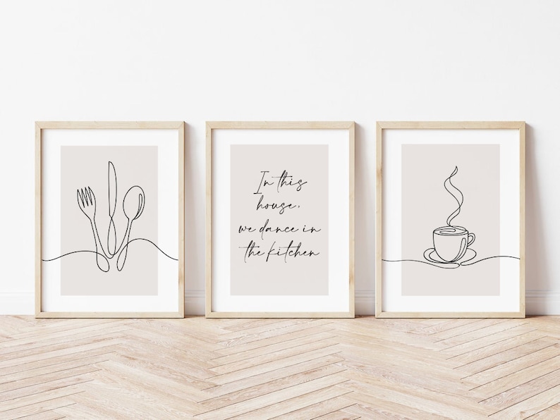 Peut inclure: Ensemble de trois impressions d'art encadr&eacute;es avec des dessins au trait minimalistes. L'une repr&eacute;sente une fourchette, un couteau et une cuill&egrave;re. Une autre dit "In this house, we dance in the kitchen." La troisi&egrave;me repr&eacute;sente une tasse de caf&eacute;.
