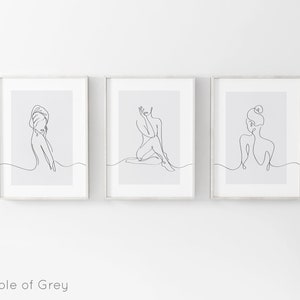 May include: Three minimalist line art prints featuring a single line drawing of a woman in different poses. The prints are framed in white and have a light gray background.