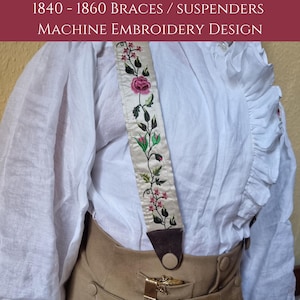 Op de afbeelding: Een paar witte stoffen bretels met een bloemenborduursel. De borduurwerk heeft roze en groene bloemen en bladeren op een crème achtergrond. De bretels zijn bevestigd aan een bruin leren band met een metalen gesp.