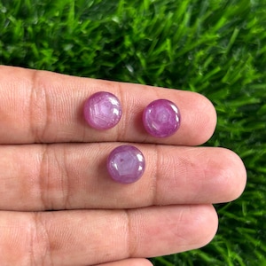 Peut inclure: Trois pierres précieuses roses rondes et polies avec des motifs en forme d'étoile sont présentées. Les pierres sont posées sur un fond d'herbe verte. Les pierres précieuses sont d'une couleur rose vif.