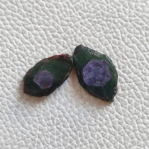 May include: Two green and purple gemstone cabochons with a faceted cut. The stones are oval shaped and have a dark green exterior with a purple centre.