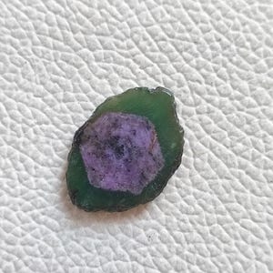 Może przedstawiać: Zielono-fioletowy kamień szlachetny z unikalnym, warstwowym wzorem. Kamień szlachetny ma owalny kształt i gładką, wypolerowaną powierzchnię.