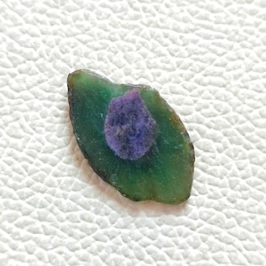 May include: A green and purple gemstone with a unique pattern. The gemstone is irregularly shaped and has a smooth, polished surface.