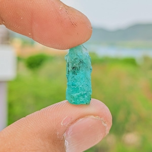 Op de afbeelding: Een ruw, ongepolijst smaragdkristal met een levendige blauwgroene tint en een zeshoekige kolomstructuur. De edelsteen heeft natuurlijke oppervlaktestructuren, zichtbare interne insluitingen en doorschijnende randen die het licht vangen.