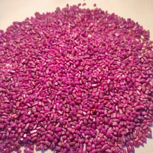 Op de afbeelding: Een close-up van een stapel ruwe, ongeslepen robijn edelstenen. De edelstenen hebben een diepe, levendige roze-rode kleur, met een ruwe, kristallijne textuur. De edelstenen zijn klein en onregelmatig van vorm.
