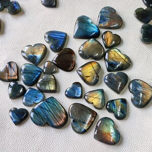 May include: A collection of heart-shaped labradorite gemstones in various shades of blue, green, and gold. The stones are polished and have an iridescent sheen.