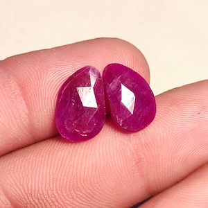 May include: Two faceted pink ruby gemstones in a pear shape.
