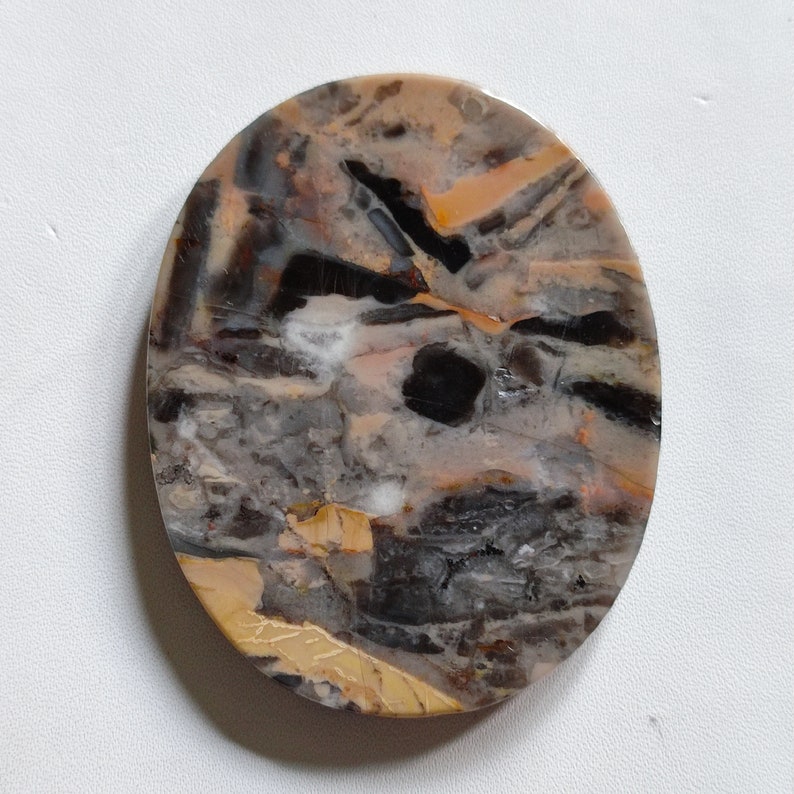 May include: A round, polished stone with a unique pattern of black, brown, and white. The stone has a natural, organic look and would be a great addition to any rock collection.