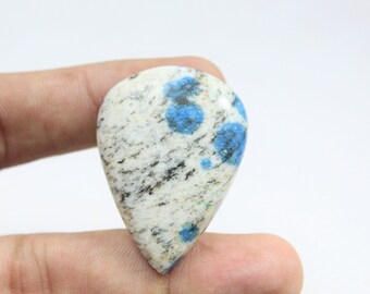 May include: A teardrop-shaped cabochon of blue kyanite in a white matrix. The stone has a speckled appearance with blue and white spots.