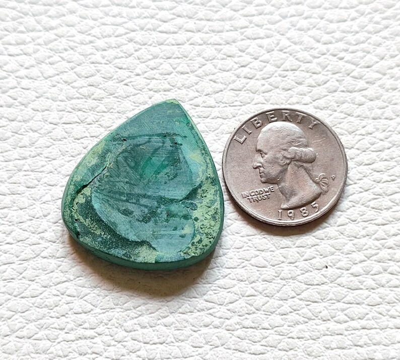 May include: A green malachite guitar pick shaped like a triangle. The pick is about the size of a US quarter.