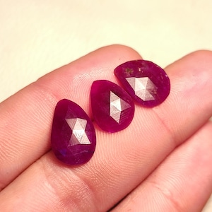 May include: Three faceted pear-shaped ruby gemstones in a deep pink colour.