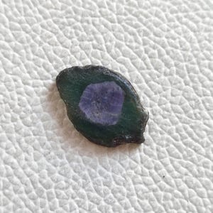 Può includere: Un piccolo sasso di forma irregolare, verde e viola, con una texture ruvida e naturale.