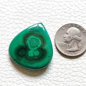 May include: A green malachite gemstone cabochon in a teardrop shape. The stone has a swirling pattern of dark green and light green.