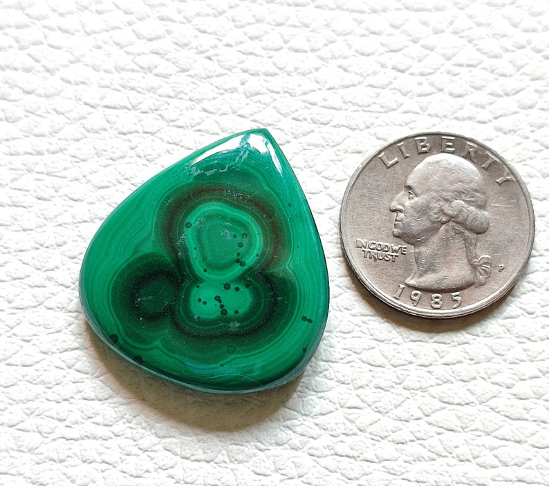 May include: A green malachite gemstone cabochon in a teardrop shape. The stone has a swirling pattern of dark green and light green.